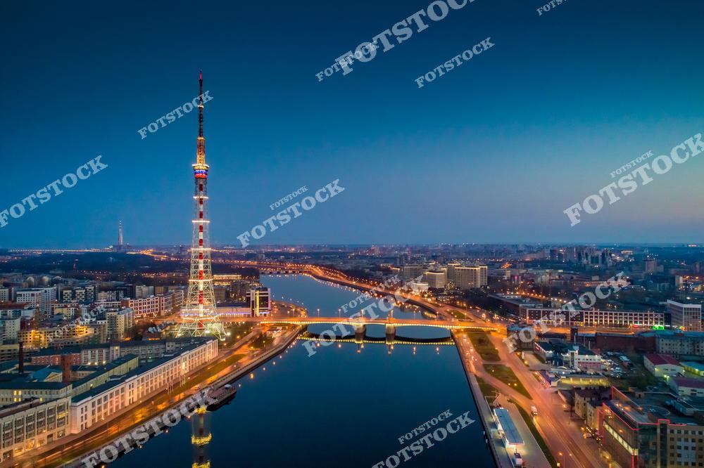 На фотографии запечатлена ночная панорама Санкт-Петербурга с видом на Санкт-Петербургскую телебашню. В кадре виден Кантемировский мост, соединяющий берега реки Невы, подсвеченный огнями. Улицы города сияют в ночной иллюминации, создавая уютную атмосферу. Это вид отражает уникальный облик ночного Петербурга, где современные элементы гармонично сочетаются с классической архитектурой.